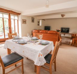 A dining table set with plates and glasses and wooden chairs next to a living area with leather sofas and a television at The Barn in Abergavenny