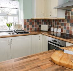 A kitchen with wooden countertops cutting board with bread and knife tiled backsplash and window at Preswylfa in Penmachno