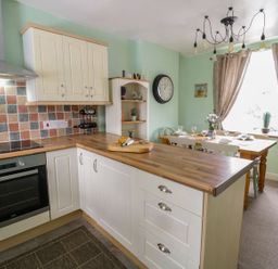 A kitchen with wooden countertops white cabinets a dining table with chairs and a large window with curtains at Preswylfa in Penmachno