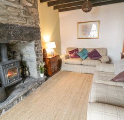 A living room with two sofas a wood burning stove a rug and side tables at Preswylfa in Penmachno