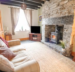 A living room with a plaid sofa cushions window with curtains stone fireplace wood stove television on wooden stand and wooden furniture at Preswylfa in Penmachno