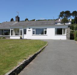 A single-story house with white walls and stone details viewed from the driveway at Cae Glas in Pwllheli