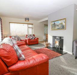 A living room with red leather sofas a wood-burning stove and a framed painting above it at Cae Glas Pwllheli