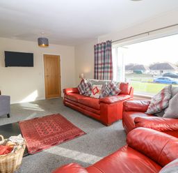 A living room with red leather sofas a red rug a basket a wall-mounted tv and large windows at Cae Glas in Pwllheli