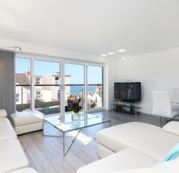 A living room with white sofas glass coffee table and TV near large windows at An Drowes in Newquay