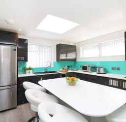 A modern kitchen with stainless steel fridge white island and stools and turquoise backsplash at An Drowes in Newquay