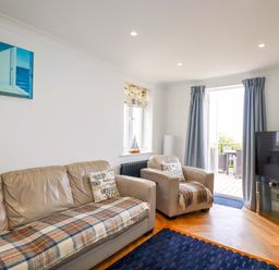 A living room with beige sofas a television and an open door leading to an outdoor seating area at Pink House in Mevagissey