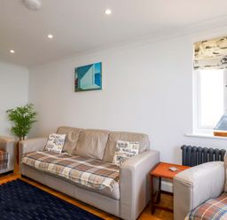 A sitting room with beige sofas and plaid blankets with cushions and a plant near the wall at Pink House in Mevagissey