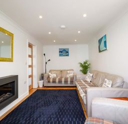 A living room with sofas, a blue rug, a wall-mounted fireplace, a yellow-framed mirror, and paintings at Pink House in Mevagissey