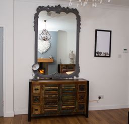 A wooden cabinet with a decorative mirror above and two grey doors on either side at Seashell Cottage in Amble-By-The-Sea