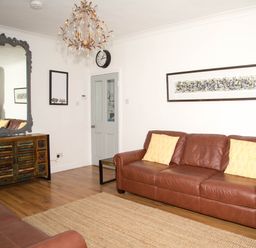 A living room with brown leather sofas yellow pillows a large mirror on a wooden cabinet and a chandelier at Seashell Cottage in Amble-By-The-Sea