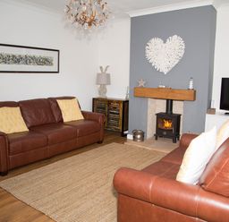 A living room with two brown leather sofas a fireplace and a television at Seashell Cottage in Amble-By-The-Sea