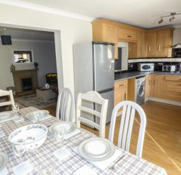 A kitchen and dining area with wooden cabinets a dining table set with plates and glasses and a living room with a fireplace in the background at Oakdene in Neyland