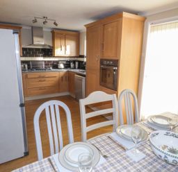 A kitchen and dining area with wooden cabinets a dining table set with plates and glasses at Oakdene in Neyland