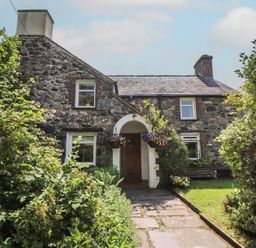 A stone house with a garden and pathway at Plas Mawr in Groeslon