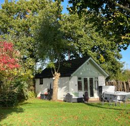 A small house with a garden seating area and trees at Pheasant Lodge in Wimborne Minster