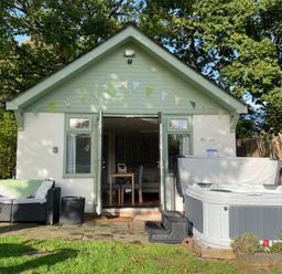 A small house with open double doors a hot tub and a sofa in the garden at Pheasant Lodge in Wimborne Minster