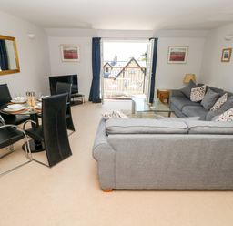 A living room with two grey sofas a glass coffee table and a dining table with black chairs at 24 Rhodewood House in Saundersfoot