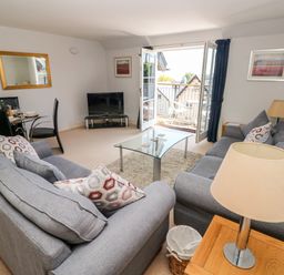 A living room with two grey sofas a glass coffee table a TV and an open balcony door at 24 Rhodewood House in Saundersfoot
