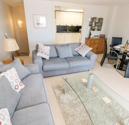 A living room with gray sofas and a glass coffee table near a dining area with black chairs at 24 Rhodewood House in Saundersfoot