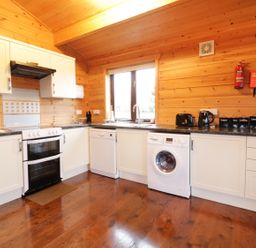 A kitchen with white cabinets black countertop a stove refrigerator dishwasher washing machine and wooden walls at Holly Lodge Lanivet near Bodmin