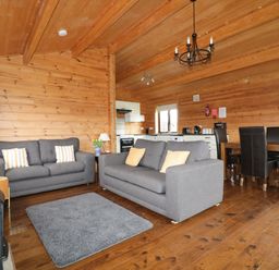 A living area with two gray sofas a gray rug a wooden dining table with six black chairs and a kitchen in a wooden cabin at Holly Lodge Lanivet near Bodmin