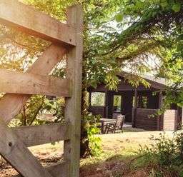 An outdoor wooden gate opening to a garden area with a wooden house and patio furniture at Hazel Lodge in Lanivet near Bodmin