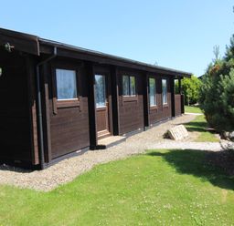 A dark wooden cabin with windows and a door surrounded by grass and trees at Hazel Lodge in Lanivet near Bodmin
