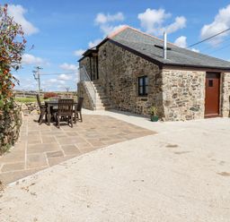 An exterior view of a stone house with a wooden door and window a patio with a table and chairs and outdoor stairs at Sunnywell in Lanivet near Bodmin