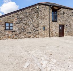 A stone building with a brown door a window and a small balcony at Sunnywell in Lanivet near Bodmin