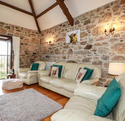 A living room with cream leather sofas green cushions a small wooden side table with a bottle and glasses stone walls and wooden ceiling beams at Sunnywell Lanivet near Bodmin