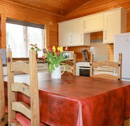 A kitchen with wooden chairs and table with flowers in a vase on the table at Cherry Lodge in Lanivet near Bodmin