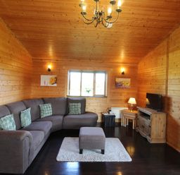 A living room with a gray corner sofa a small ottoman a tv on a wooden cabinet and wooden walls at Cherry Lodge in Lanivet near Bodmin