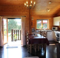 An open plan kitchen and dining area with wooden walls and ceiling a dining table with chairs and a kitchen with white cabinets at Cherry Lodge Lanivet near Bodmin