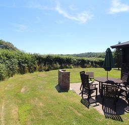 A garden with a patio table and chairs with an umbrella near a wooden structure at Maple Lodge in Lanivet near Bodmin