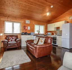A living area with leather armchairs a rug a kitchen with white cabinets and appliances at Cedar Lodge in Lanivet near Bodmin