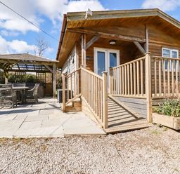 An outdoor area with a wooden cabin featuring a ramp and a patio with a covered seating area at Hunrosa in St Day