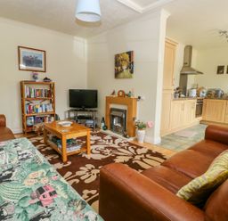 A living room with a sofa bookshelf TV and an open kitchen at Richmond Cottage in Burythorpe near Malton