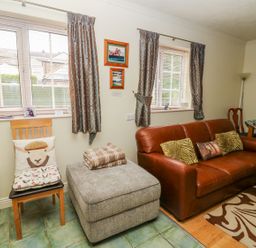 A living room with a brown leather sofa and cushions a grey ottoman with blankets and chairs near windows with curtains at Richmond Cottage in Burythorpe near Malton