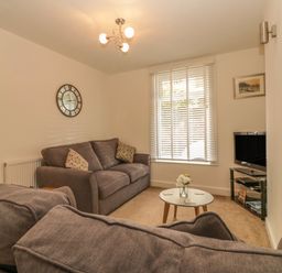 A living room with gray sofas a round coffee table a wall clock and a television at Sunvale in Teignmouth