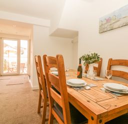 A dining area with a wooden table set with plates glasses and a bottle next to doors leading to an outdoor patio at Sunvale in Teignmouth