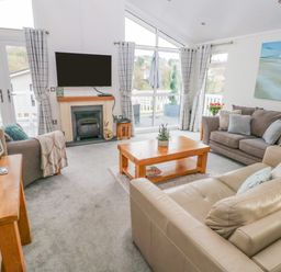 A living room with a fireplace a wall-mounted TV sofas a wooden coffee table and large windows at The Lookout in Stepaside