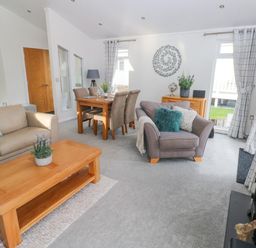 A living room with beige and gray sofas a wooden coffee table a dining table with chairs and windows with curtains at The Lookout in Stepaside