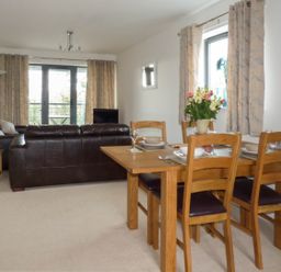 A dining table with four chairs and set tableware next to a living room with dark leather sofas and large windows at Tyack in Charlestown