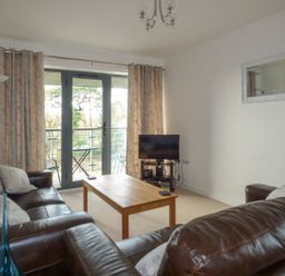 A living room with brown leather sofas a wooden coffee table a television and glass doors leading to a balcony at Tyack Charlestown