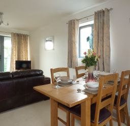 A dining table set with plates glasses and a vase of flowers next to a window with curtains and a dark sofa in a living room at Tyack in Charlestown