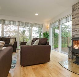 A living room with brown sofas a wood burning stove and large windows with a view of trees at Birch in Truro