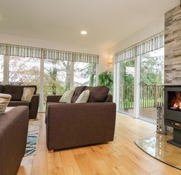A living room with brown sofas a wood burning stove and large windows overlooking trees at Elm in Truro