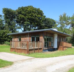 A wooden cabin with a deck and railing surrounded by grass and trees at Elm in Truro