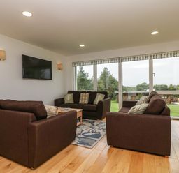 A living room with three brown sofas a wall-mounted TV and large windows showing an outdoor view at Hazel in Truro